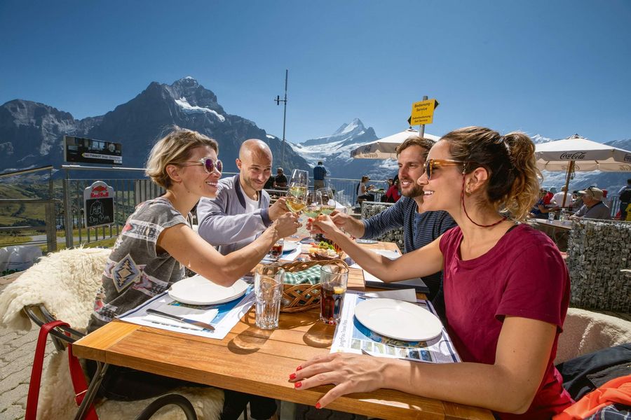 Gruppe stösst im Bergrestaurant First an und geniesst die Sonne und den Bergblick