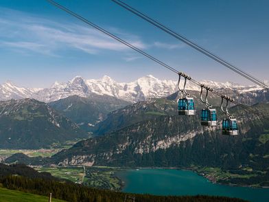 Gondeln der Niederhornbahn im Sommer mit dem Thunersee und der verschneiten Bergkette im Hintergrund