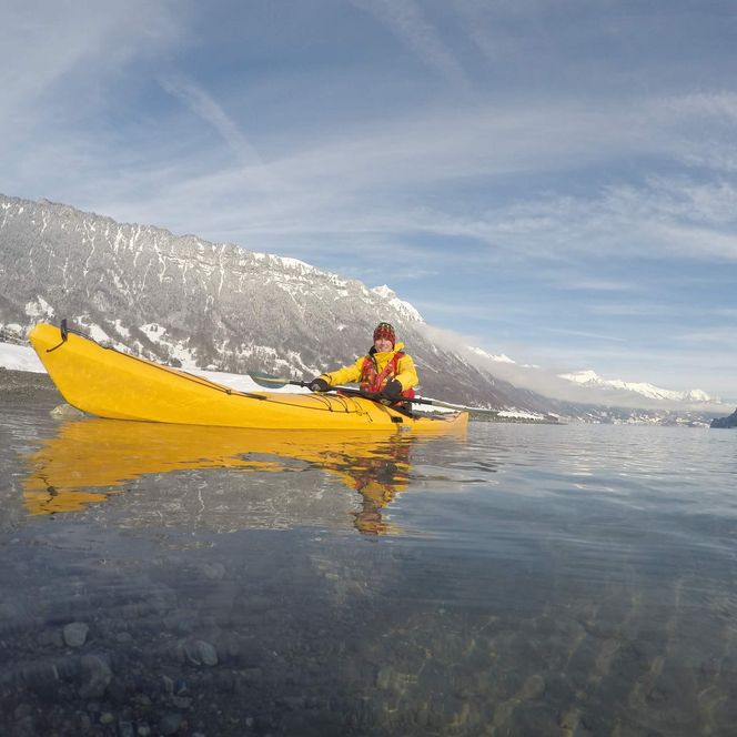 Kajakfahrer in einem gelben Kajak auf dem Brienzersee mit verschneiten Bergflanken