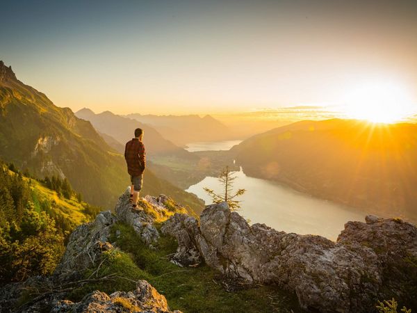 Wanderer geniesst den Sonnenuntergang über dem Thuner- und Brienzersee. Die Naturlandschaft ist in goldenes Licht getaucht.