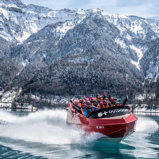 Jetboat unterwegs auf dem spiegelglatten Brienzersee im Winter mit verschneiten Wälder und Bergen