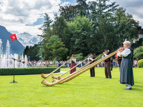 Alphornspieler auf grüner Wiese vor Wasserspiel im Kursaal Garten Interlaken