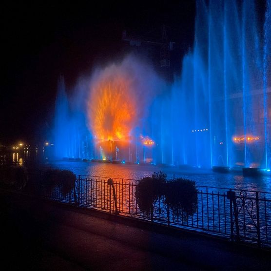 Wasserspiel mit blauen Fontänen und orangem Kreis in der Mitte am Thuner Wasserzauber auf der Aare neben dem Hotel Freienhof in Thun
