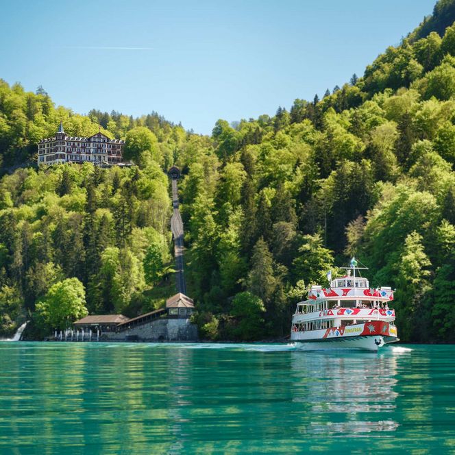 Ein Schiff auf dem türkisen Brienzersee und im grünen Wald das Grandhotel Giessbach