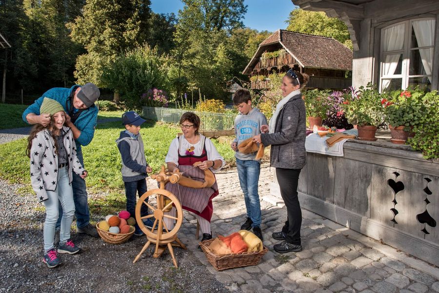 Familie schaut einer Frau beim Spinnen zu im Freilichtmuseum Ballenberg